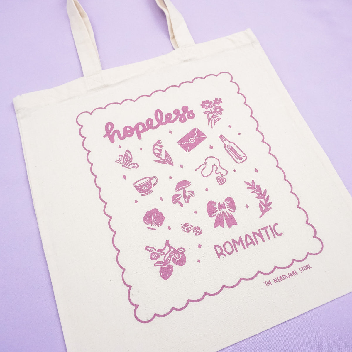 tote bag with illustrations in purple that say hopeless romantic with romantic flowers, a butterfly, mushrooms, strawberries, and a scalloped border