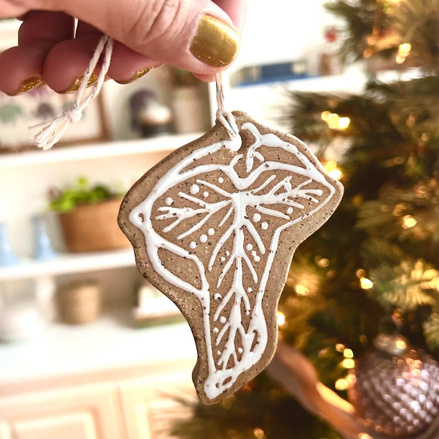 a hand holds up a brown clay ornament with white glaze in the style of a leaf of lorien brooch from the lord of the rings