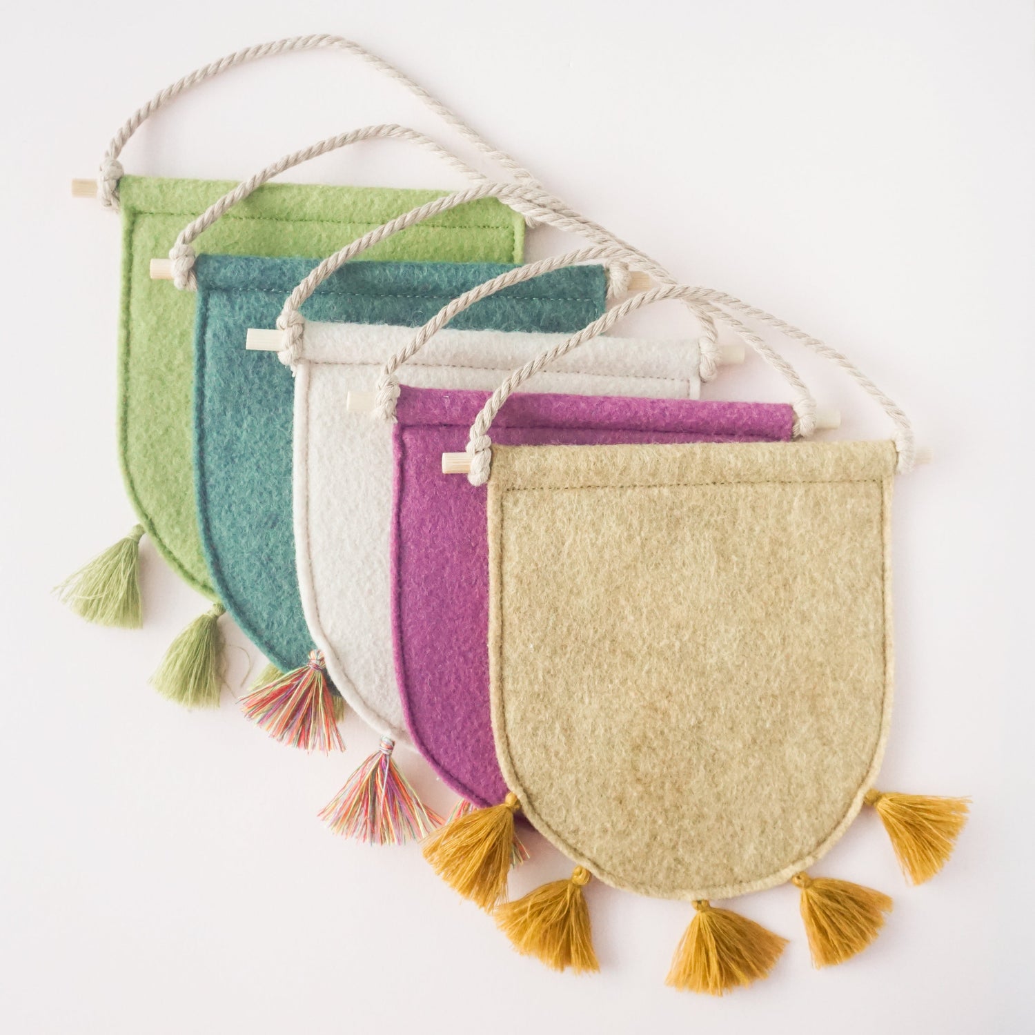 An arrangement of different colors of mini handmade pin banners made with felt and tassels on the bottom