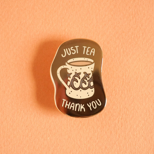 A small gold enamel pin with the words "just tea thank you" on it around a vintage style mug with tea in it.