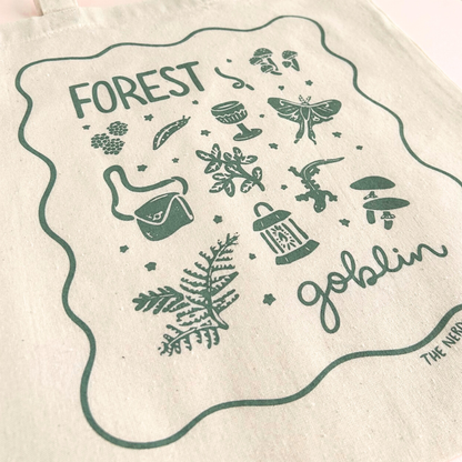 tote bag with designs in dark green that say forest goblin with fantastical illustrations of a slug, a goblet, a satchel, foliage, a lantern, mushrooms, and a luna moth