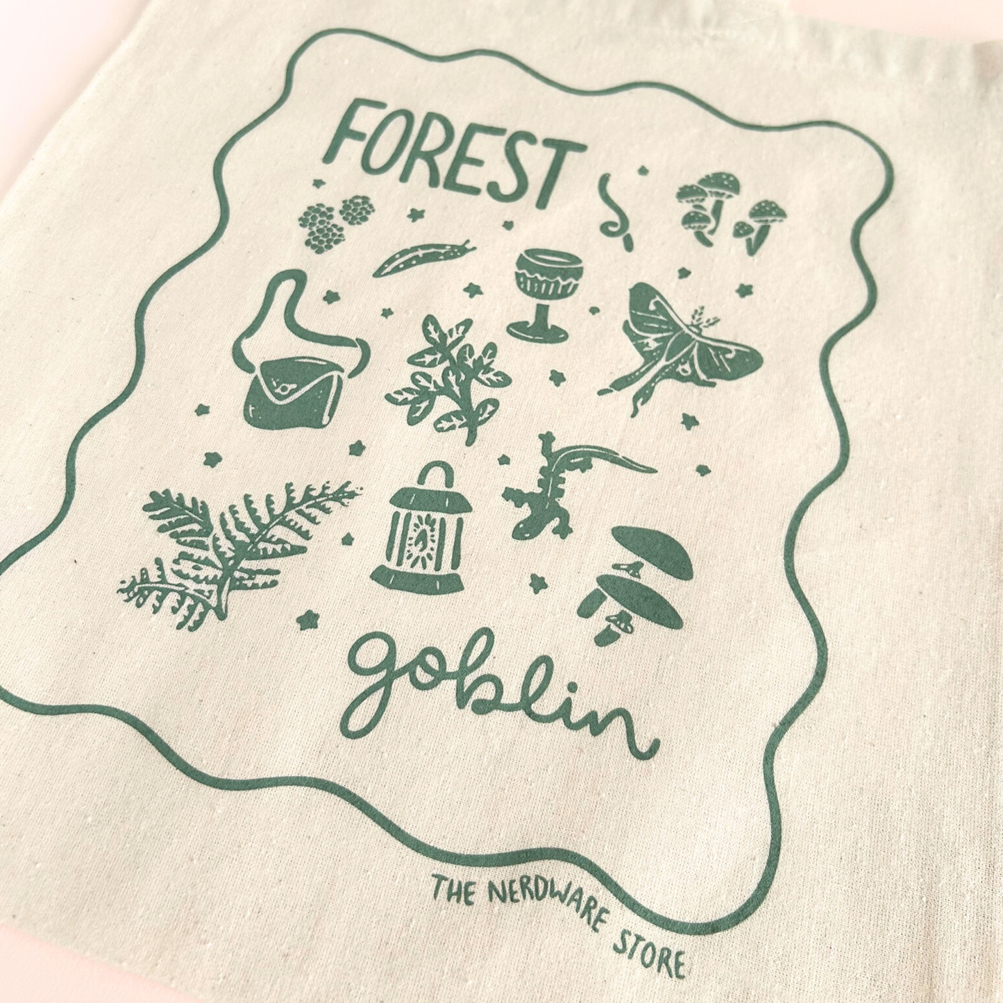 tote bag with designs in dark green that say forest goblin with fantastical illustrations of a slug, a goblet, a satchel, foliage, a lantern, mushrooms, and a luna moth