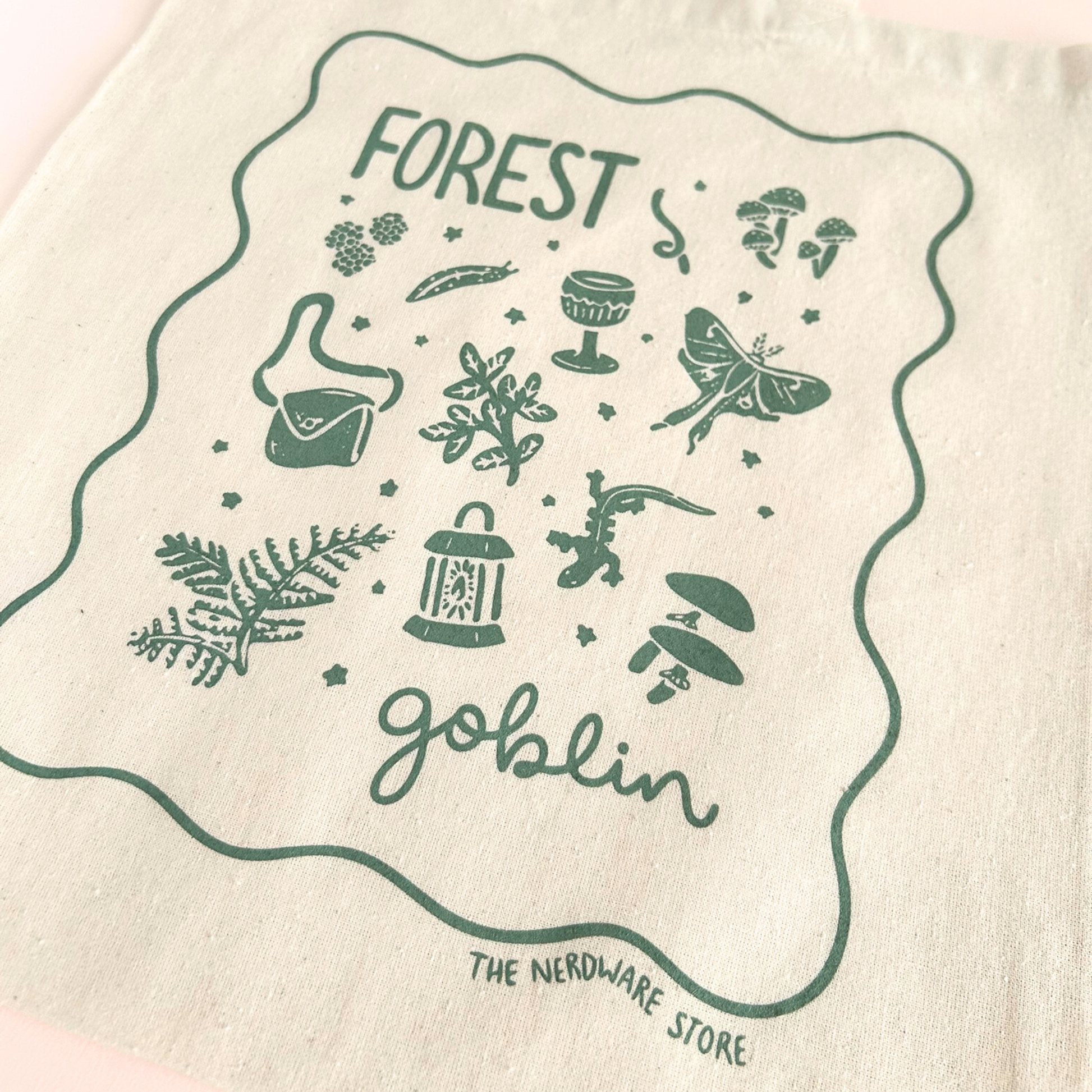 tote bag with designs in dark green that say forest goblin with fantastical illustrations of a slug, a goblet, a satchel, foliage, a lantern, mushrooms, and a luna moth