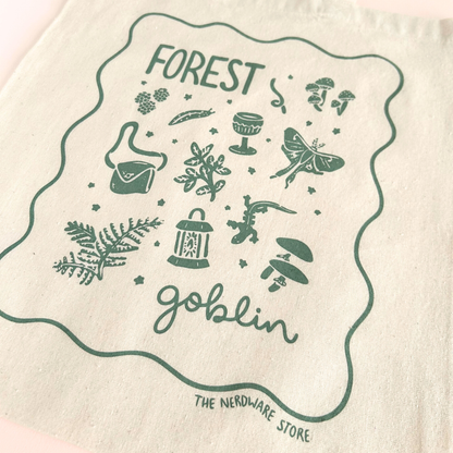 tote bag with designs in dark green that say forest goblin with fantastical illustrations of a slug, a goblet, a satchel, foliage, a lantern, mushrooms, and a luna moth