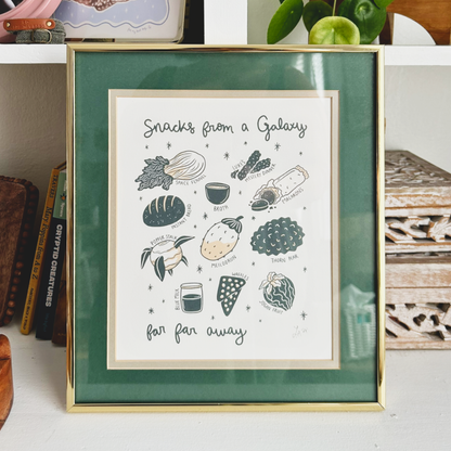 Framed artwork titled 'Snacks from a Galaxy far far away' on a shelf with books and decorative items.