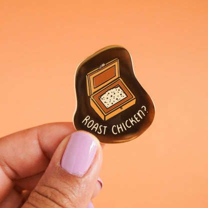 A gold enamel pin with a salt box open on the pin and the words "roast chicken?" around the salt box.