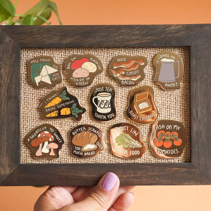 A collection of gold enamel pins with words on them and food from the lord of the rings.