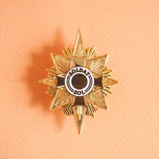 A gold star shaped enamel pin that says "soldat sol" on it.