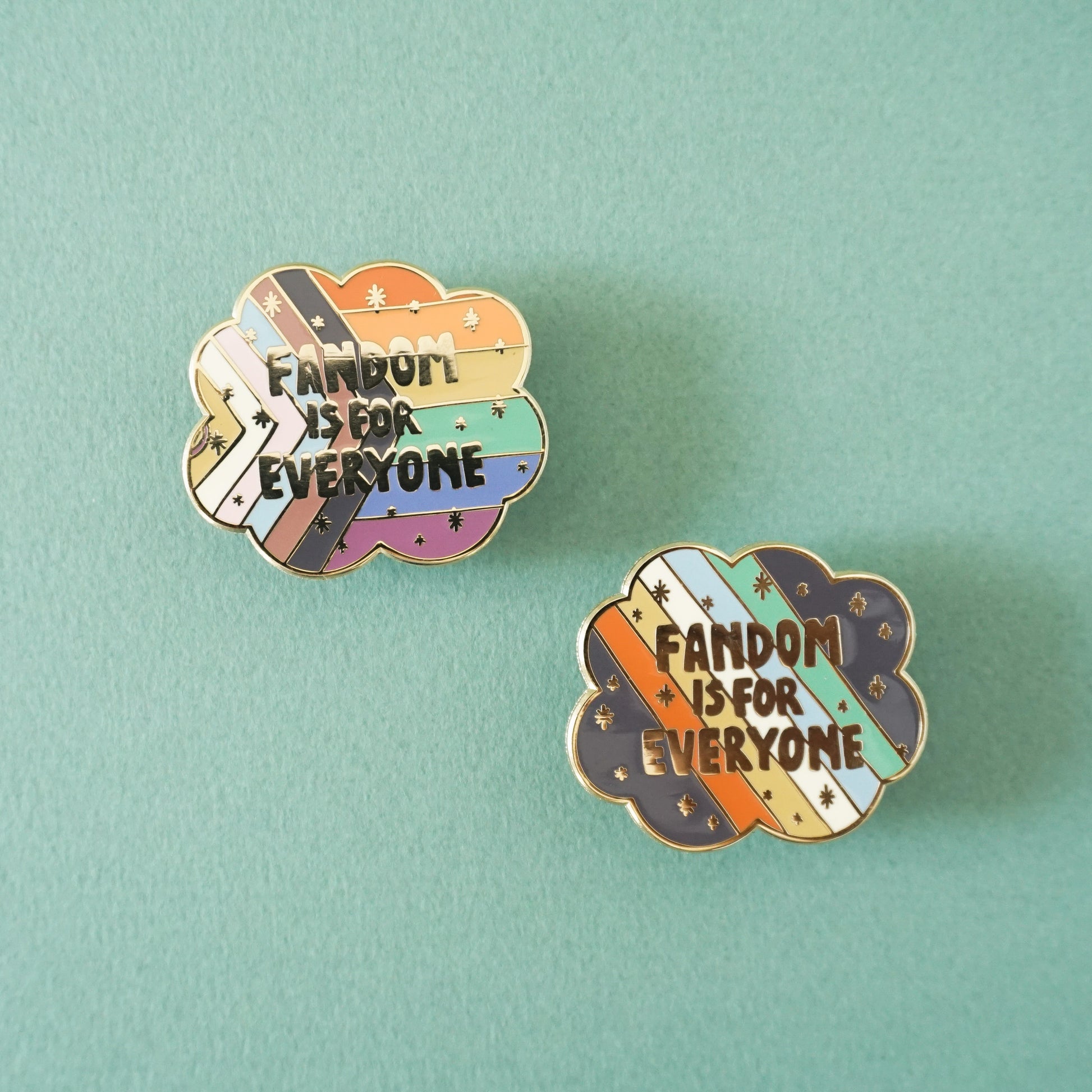 A gold enamel lapel pin showing the LGBTQIA+ pride flag with the words "Fandom is for everyone" over top.