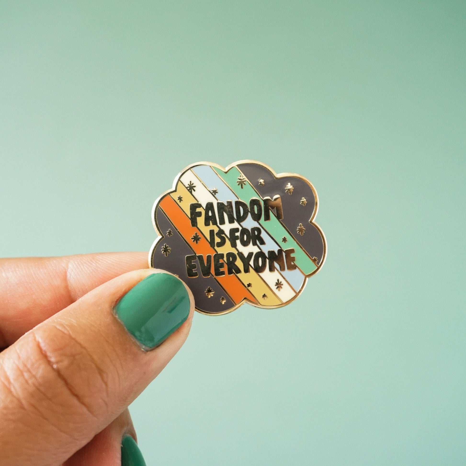 A small scallop edged enamel pin that says "fandom is for everyone" over the disability pride flag.