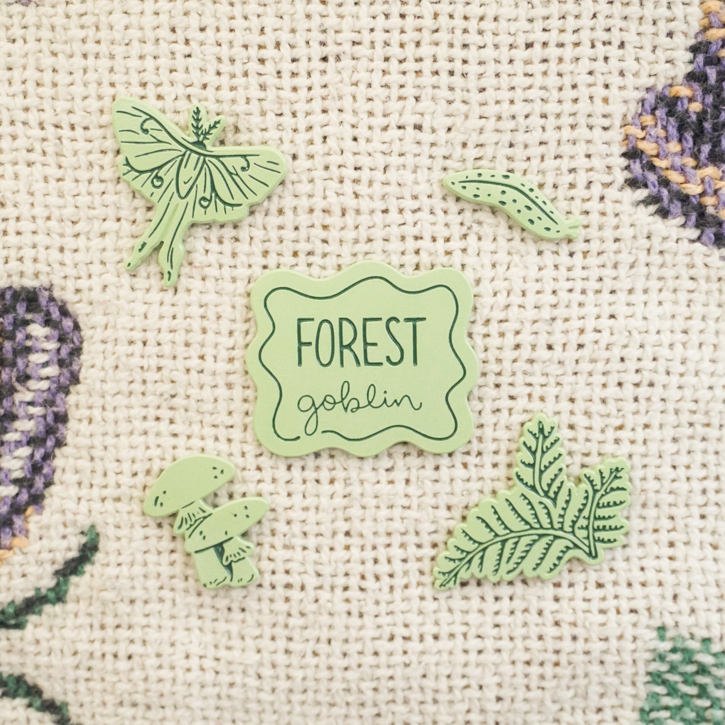 five light green pins of a slug, ferns, a luna moth, mushrooms, and a pin that says forest goblin