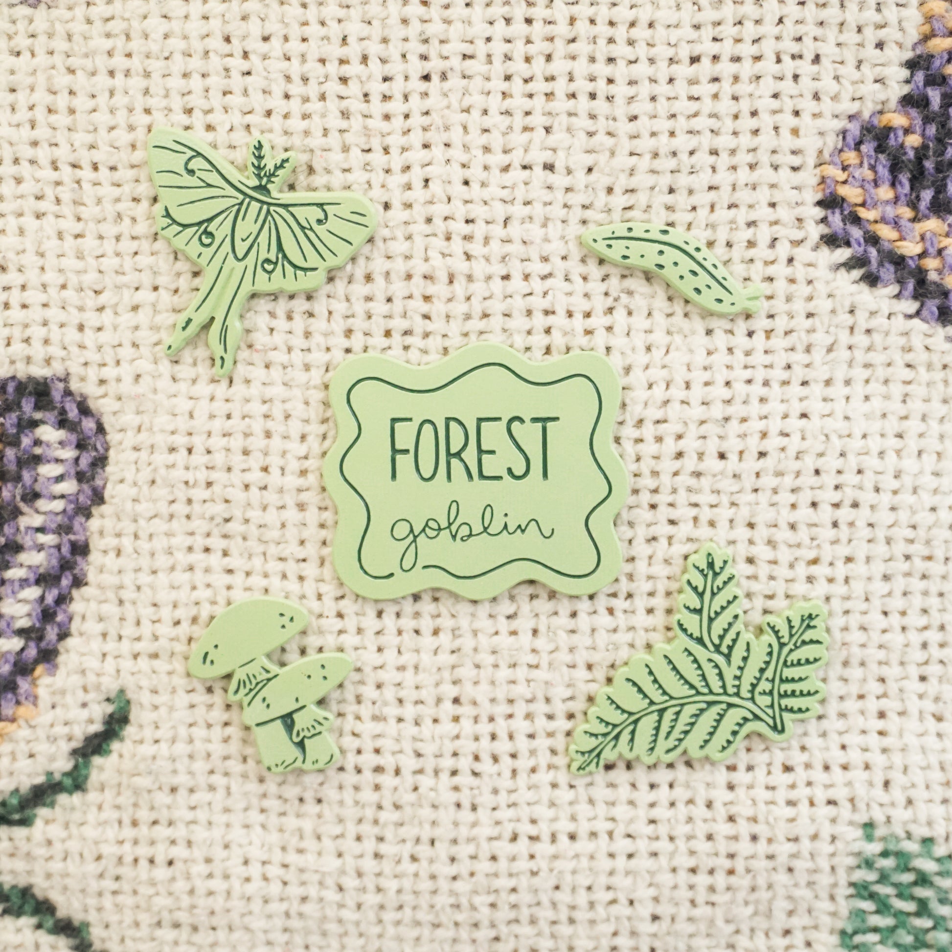 five light green pins of a slug, ferns, a luna moth, mushrooms, and a pin that says forest goblin