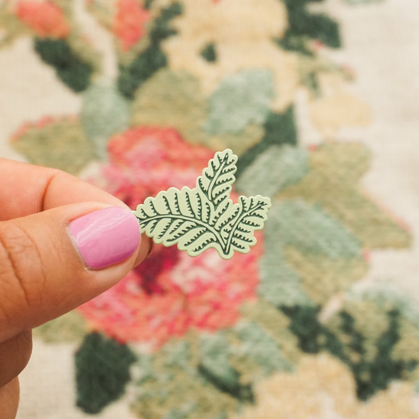 a hand holds up a mint green pin in the shape of a fern bush