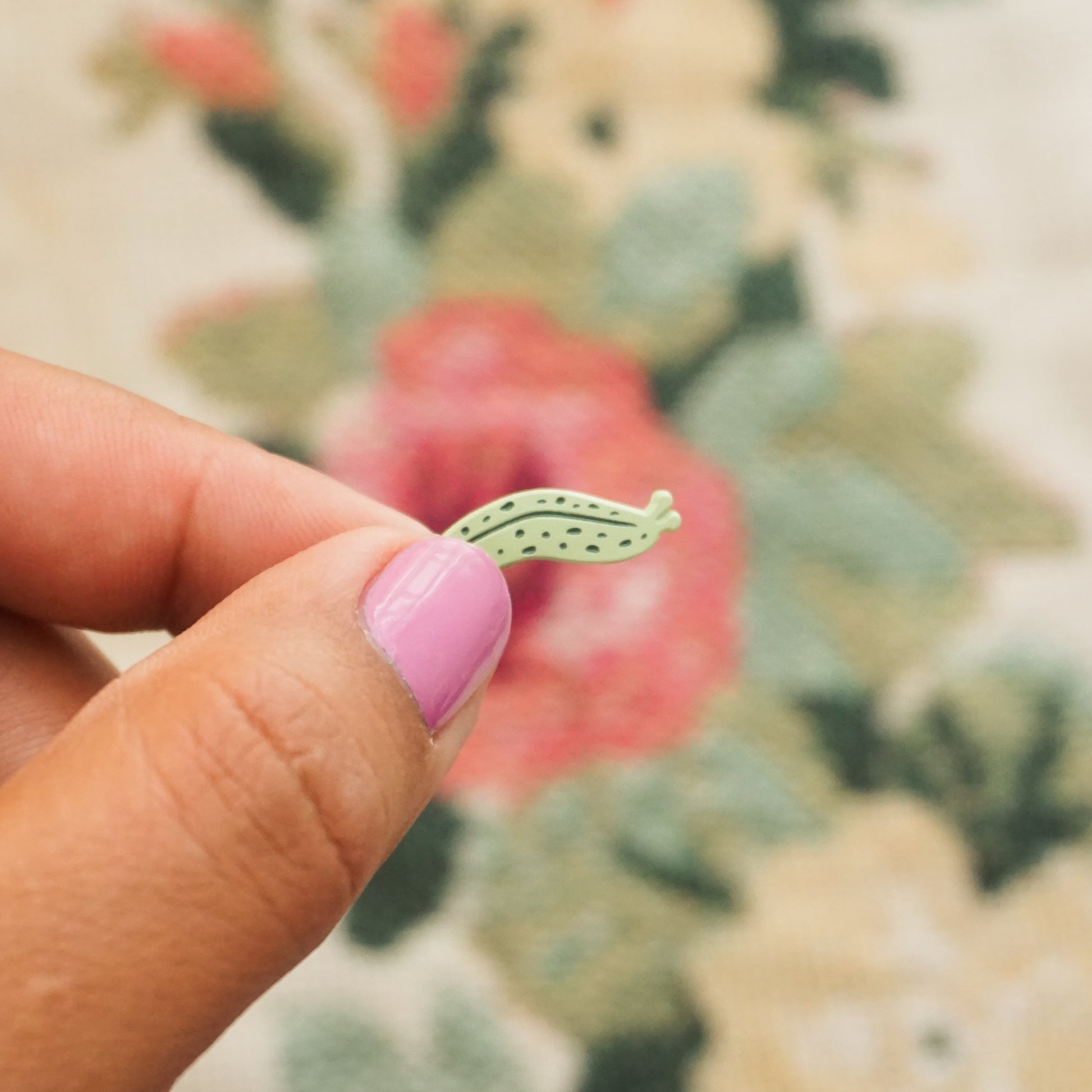 a hand holds up a mint green pin in the shape of a slug