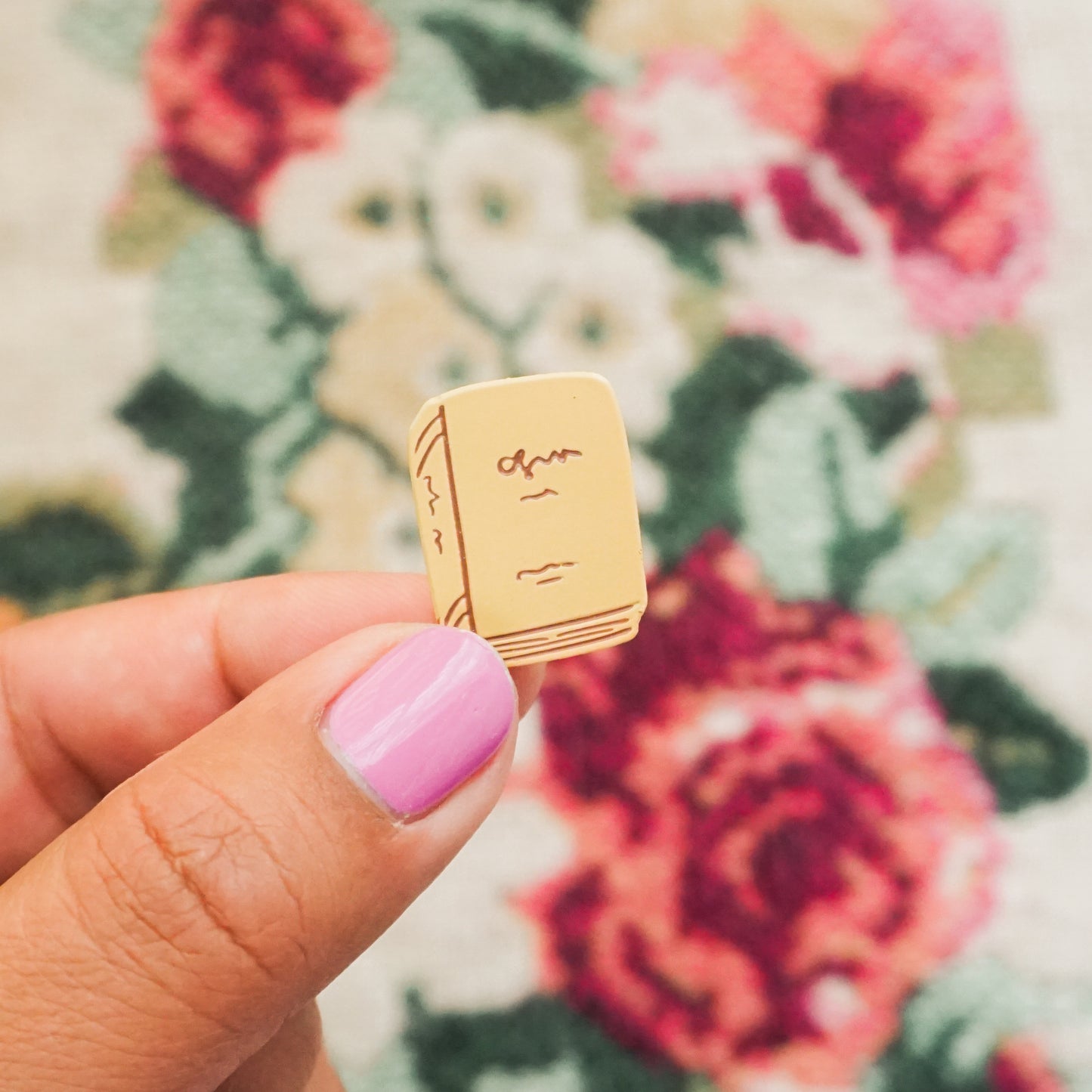 hand holding a peach colored enamel pin in the shape of a book