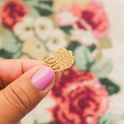 hand holding a peach colored enamel pin in the shape of a rose