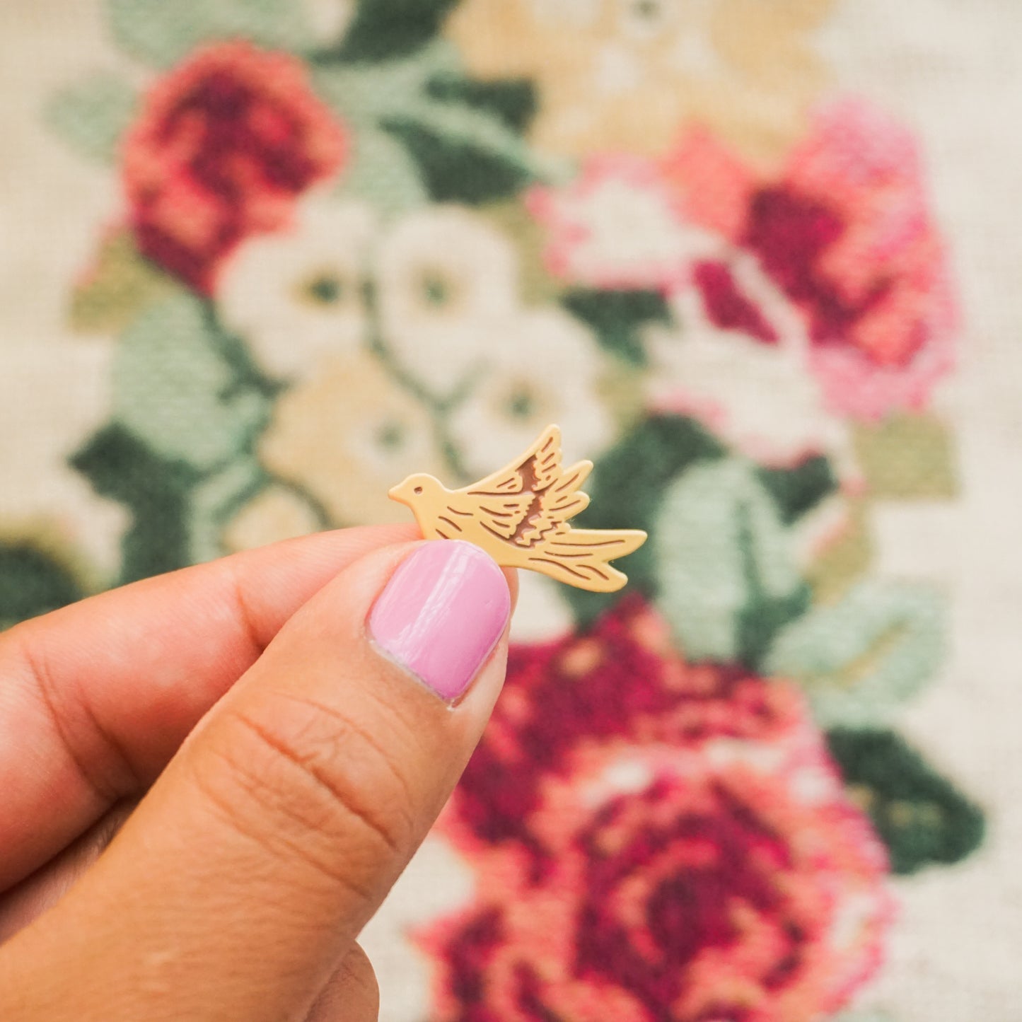 hand holding a peach colored enamel pin in the shape of a dove