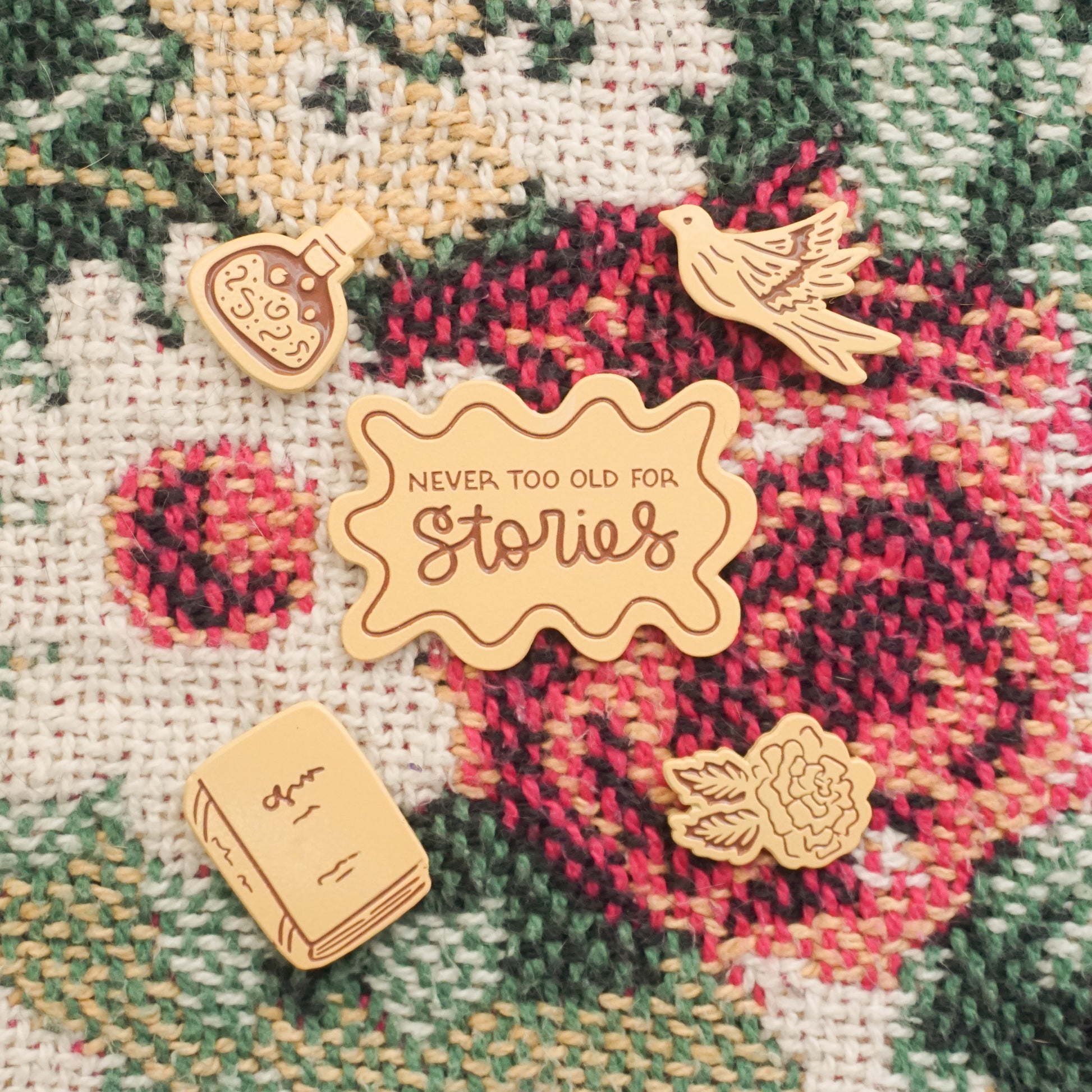 five story themed peach colored enamel pins on a floral blanket texture background