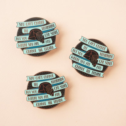 Three round black pins with a teal banner on it that says "you cannot change the beginning, but you can start where you are and changing the ending" around kylo ren's broken helmet.