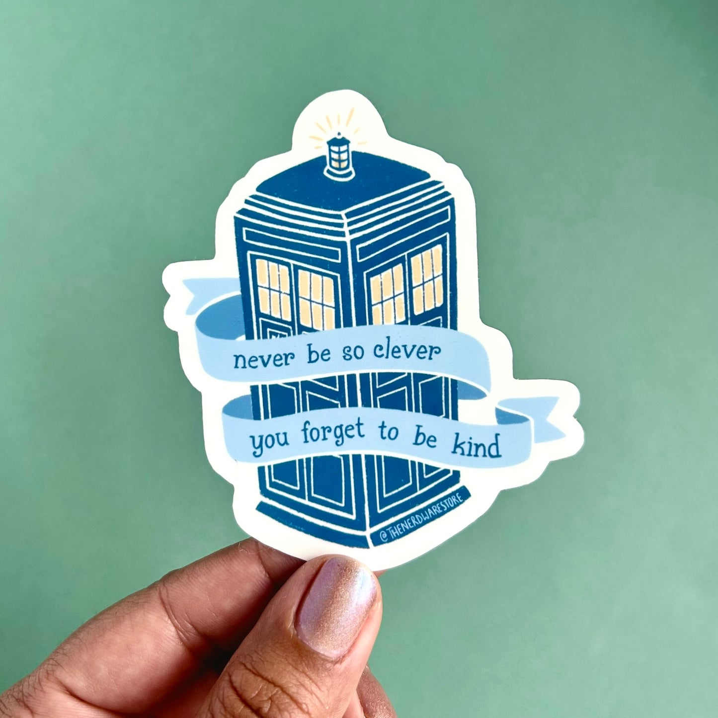 A large vinyl decal sticker of the Tardis from Doctor Who with words on a banner that say "never be to clever you forget to be kind."