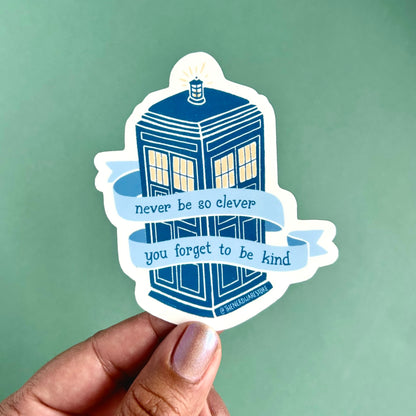 A large vinyl decal sticker of the Tardis from Doctor Who with words on a banner that say "never be to clever you forget to be kind."