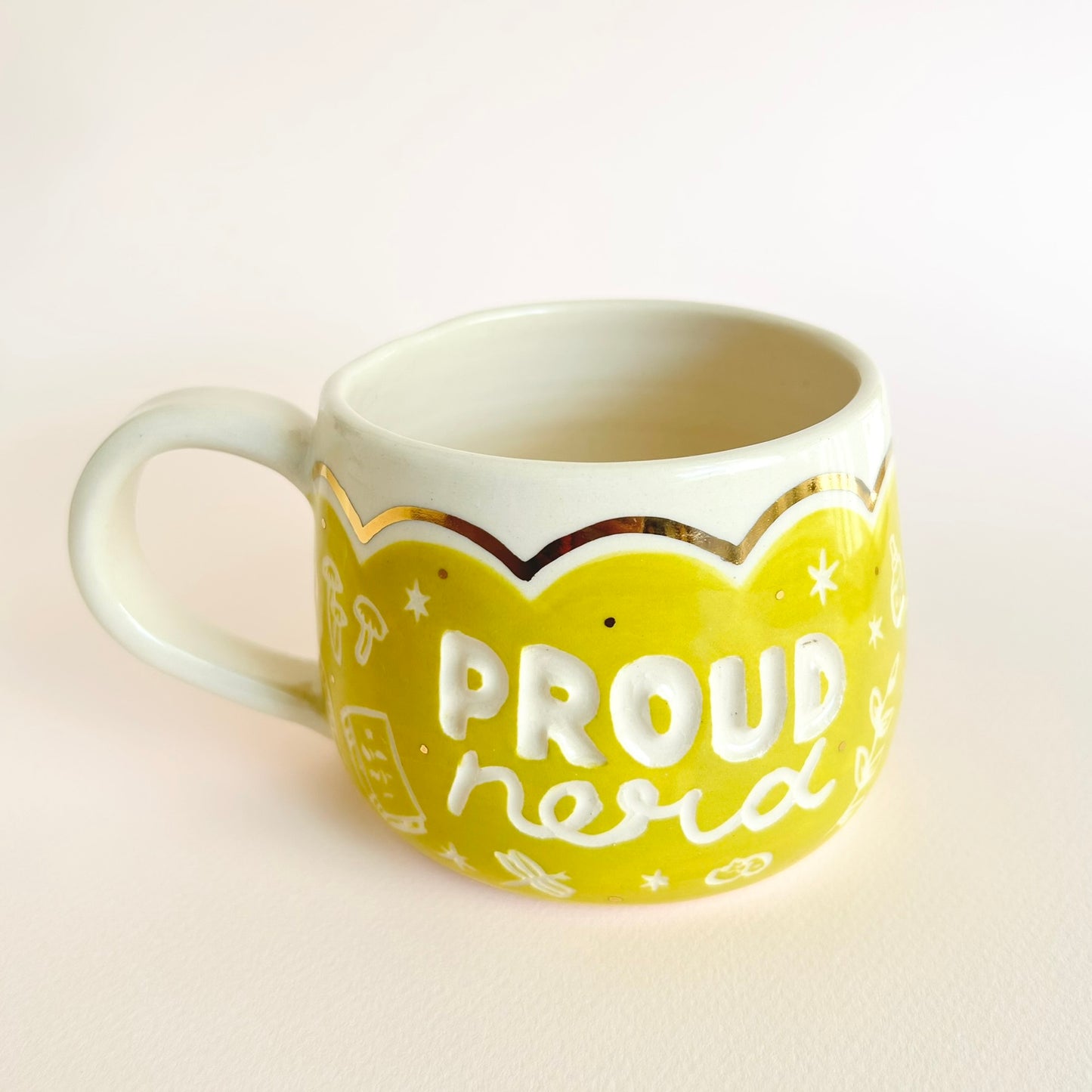 A bright chartreuse mug with the words "proud nerd" on the front and other etched items and gold scalloped details on the top