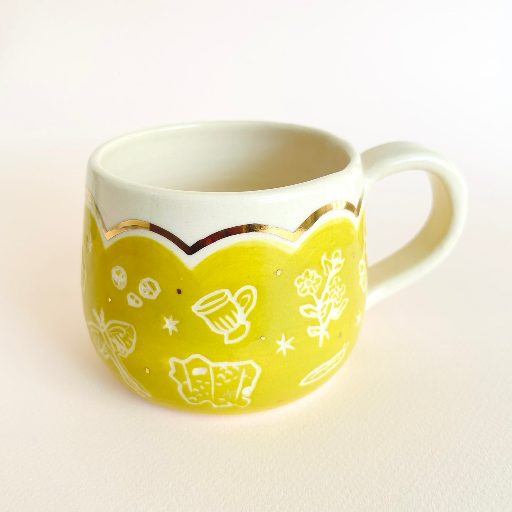 a bright yellow and chartreuse mug with flowers, a mug, a luna moth, crystals, and a map, are etched and gold scalloped details on top.