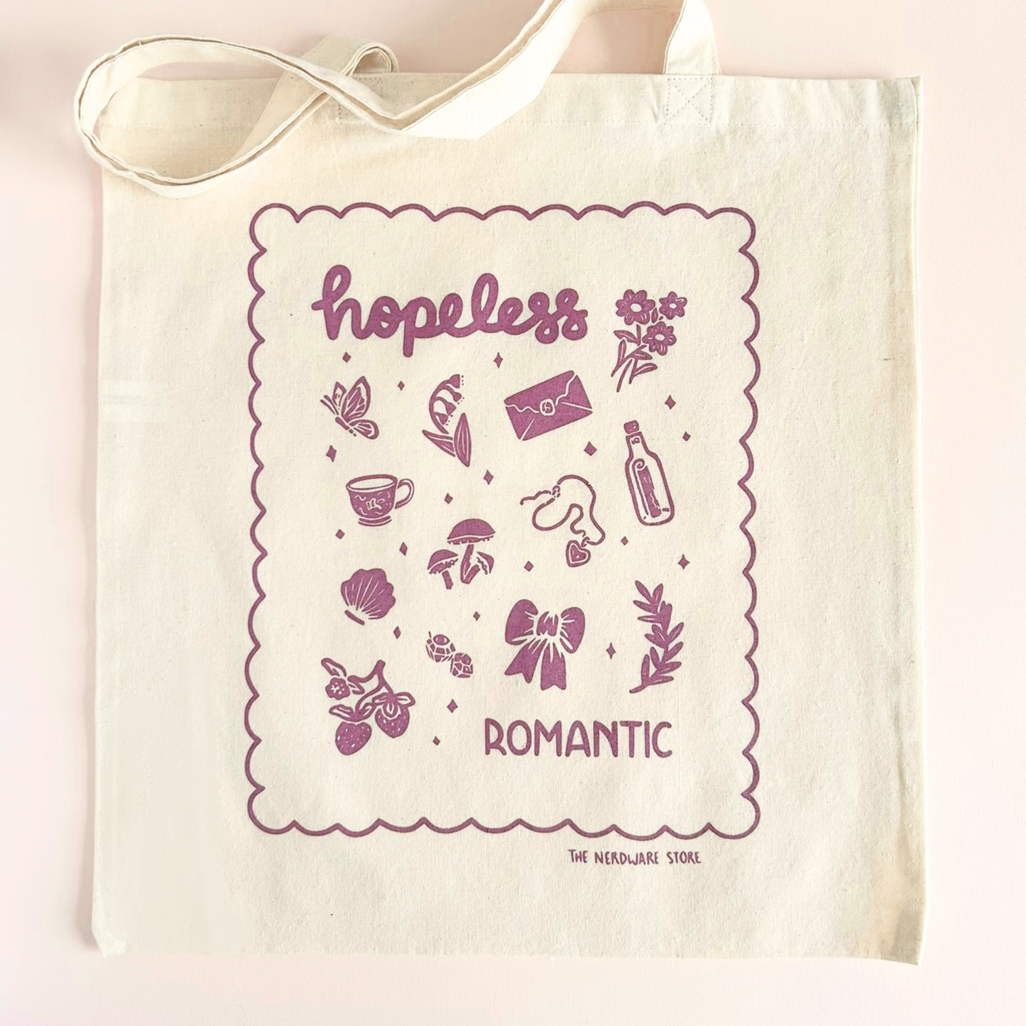 tote bag with illustrations in purple that say hopeless romantic with romantic flowers, a butterfly, mushrooms, strawberries, and a scalloped border