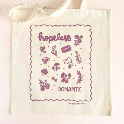tote bag with illustrations in purple that say hopeless romantic with romantic flowers, a butterfly, mushrooms, strawberries, and a scalloped border
