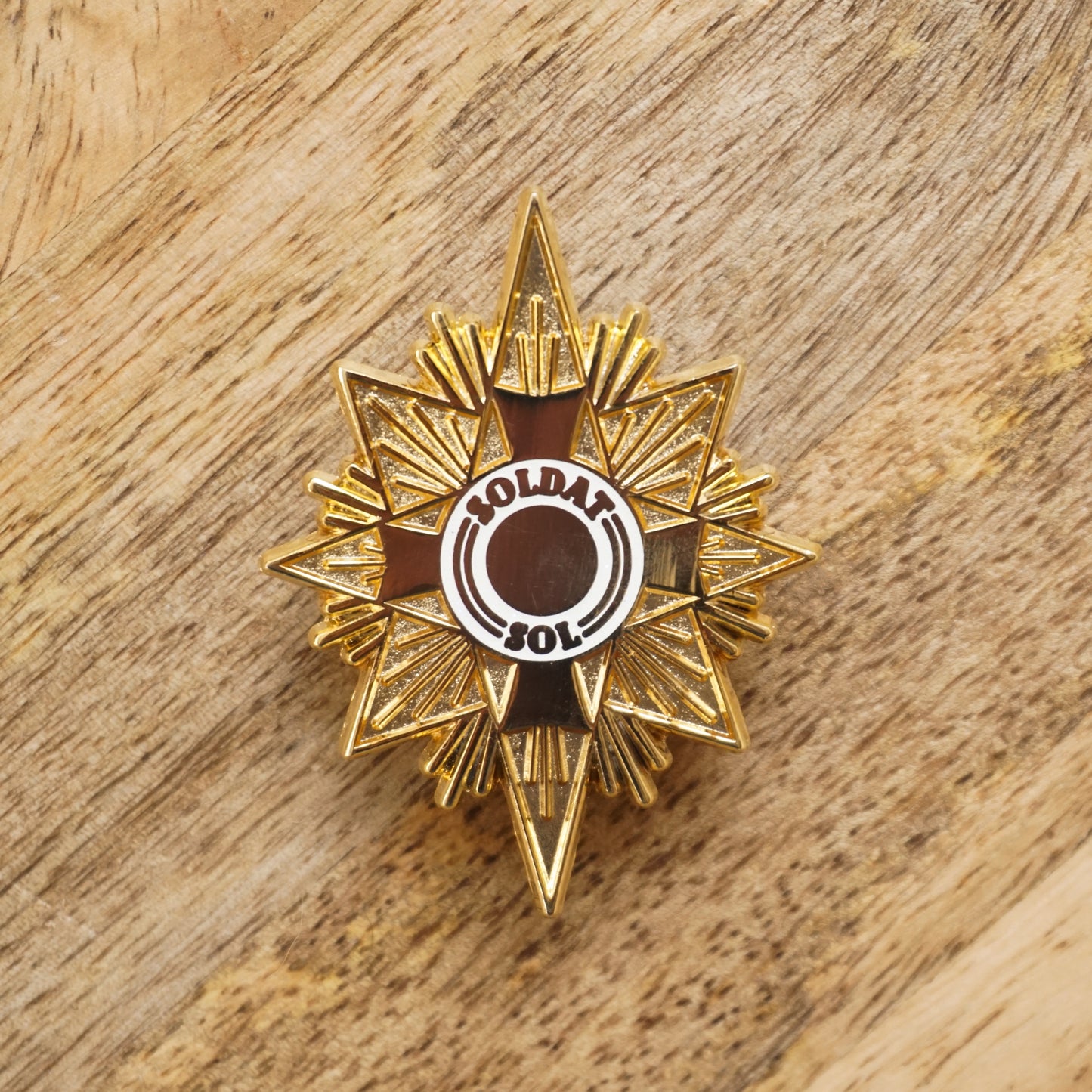 A gold star shaped enamel pin that says "soldat sol" on it.