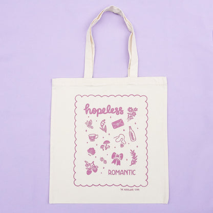 tote bag with illustrations in purple that say hopeless romantic with romantic flowers, a butterfly, mushrooms, strawberries, and a scalloped border