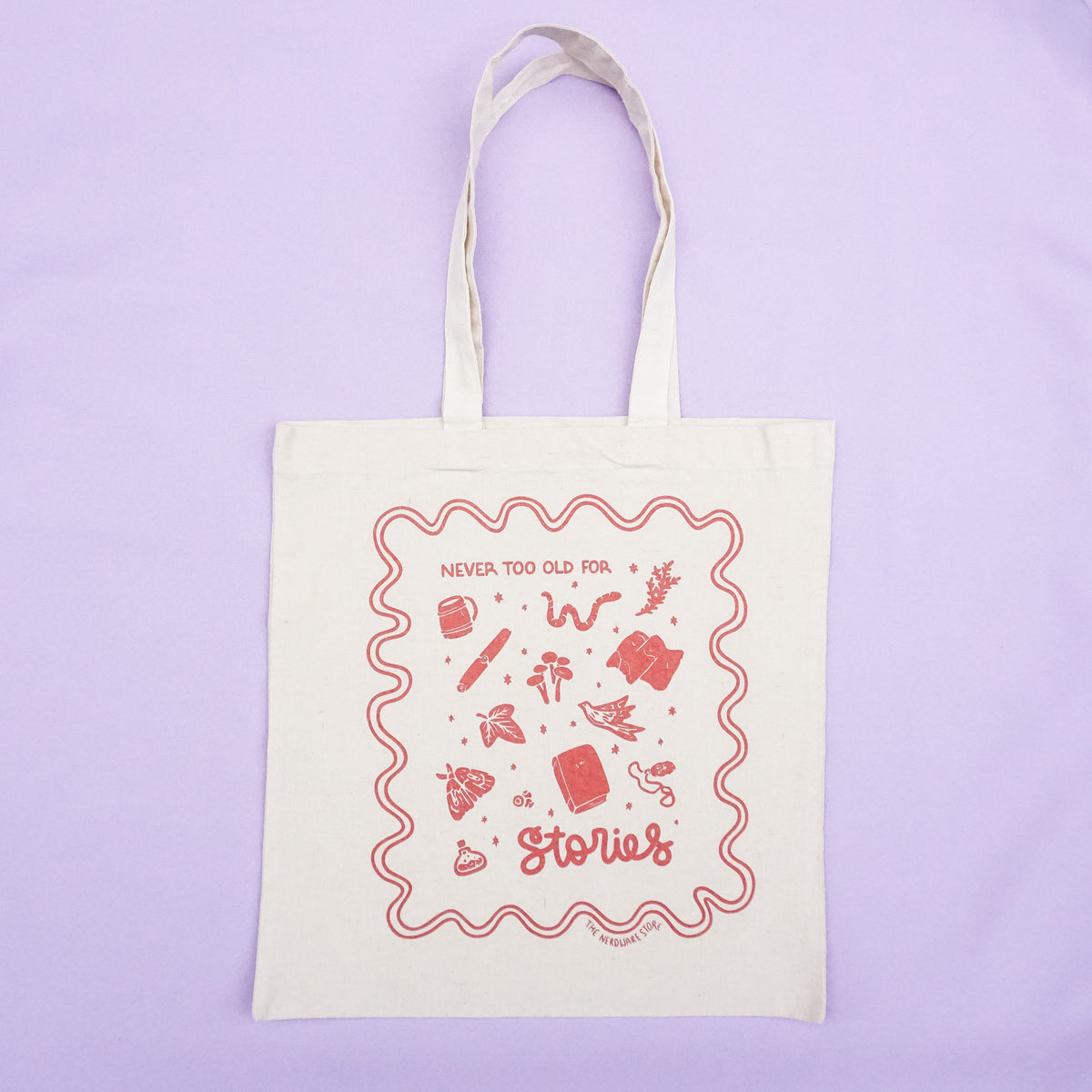 tote bag with designs in maroon that say never too old for stories with fantastical illustrations of a book, locket, moth, leaf, and more