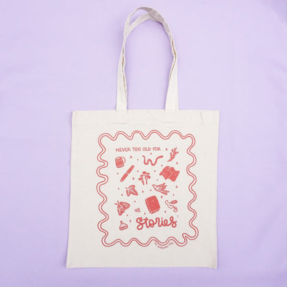 tote bag with designs in maroon that say never too old for stories with fantastical illustrations of a book, locket, moth, leaf, and more