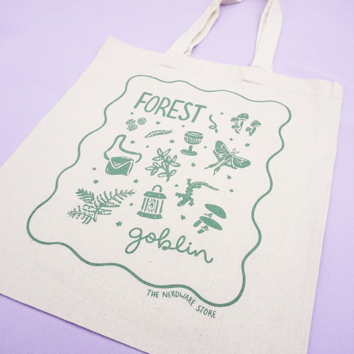 tote bag with designs in dark green that say forest goblin with fantastical illustrations of a slug, a goblet, a satchel, foliage, a lantern, mushrooms, and a luna moth