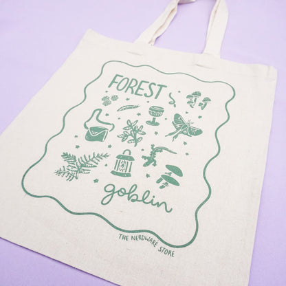tote bag with designs in dark green that say forest goblin with fantastical illustrations of a slug, a goblet, a satchel, foliage, a lantern, mushrooms, and a luna moth