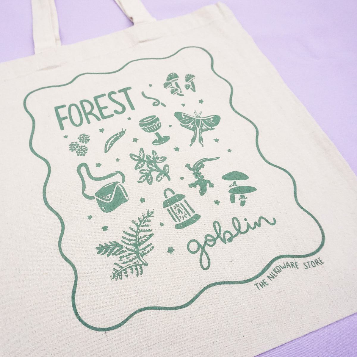 tote bag with designs in dark green that say forest goblin with fantastical illustrations of a slug, a goblet, a satchel, foliage, a lantern, mushrooms, and a luna moth