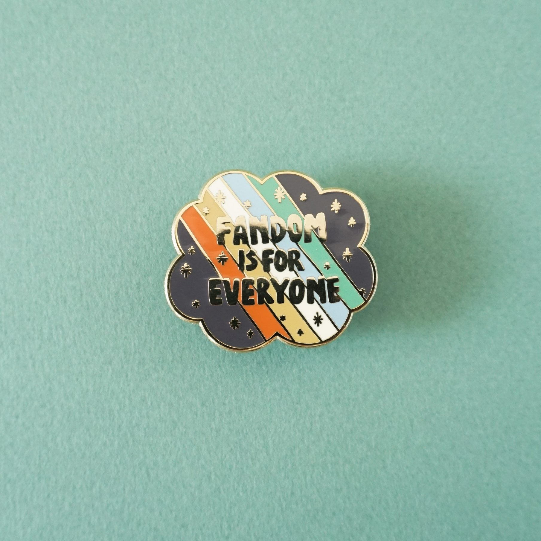 A small scallop edged enamel pin that says "fandom is for everyone" over the disability pride flag.