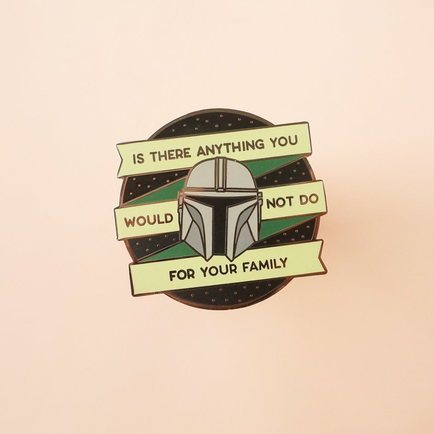 A round black pin with green banner on it that says "is there anything you would not do for your family," around Mando's helmet.