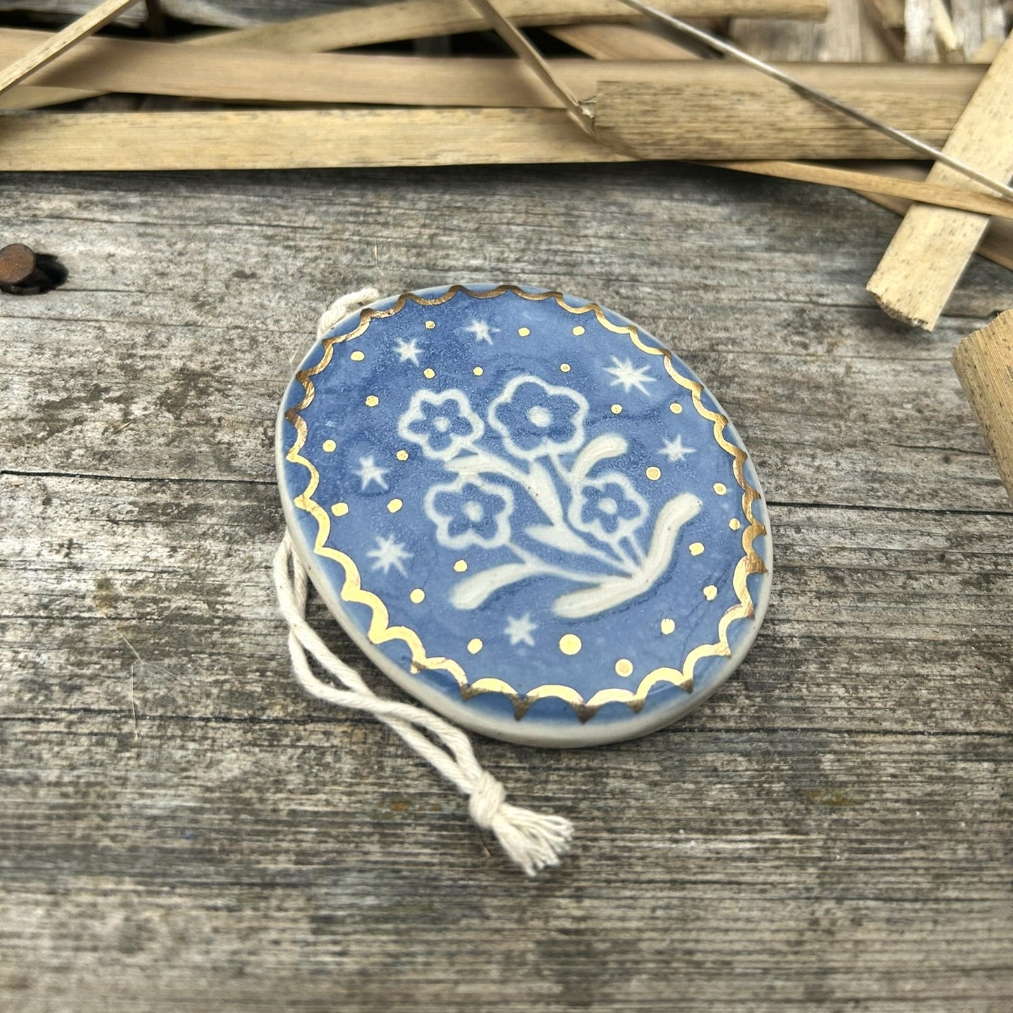 a bright blue ornament with some vintage style flowers carved into it and gold scalloped edges and gold dots