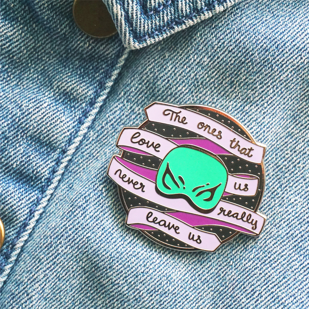 purple and green enamel pin with kanan's visor and the words "the ones that love us never really leave us." The pin is on a jean jacket.